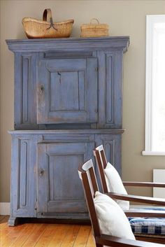 an old blue cabinet in the corner of a room with a basket on top of it