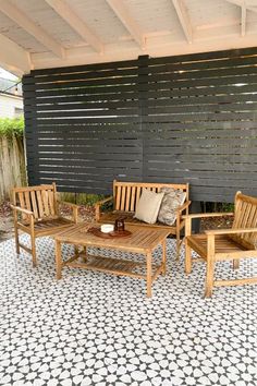 an outdoor seating area with wooden chairs and coffee table on tiled floor next to black fence