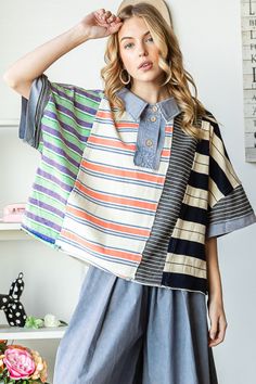 a woman standing in front of a white wall wearing a striped shirt and blue pants