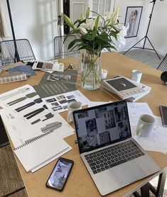 an open laptop computer sitting on top of a wooden table next to a vase filled with flowers