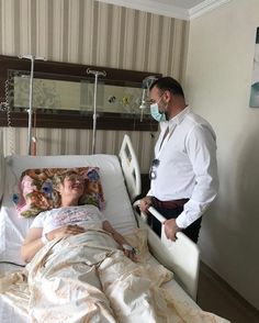 a man standing next to a woman laying in a hospital bed with oxygen mask on