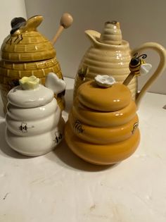 three ceramic honey pots and a beehive are sitting on a counter top next to each other