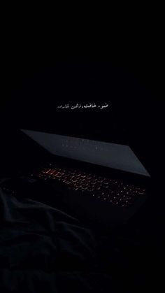 an open laptop computer sitting on top of a bed in the dark with arabic writing above it