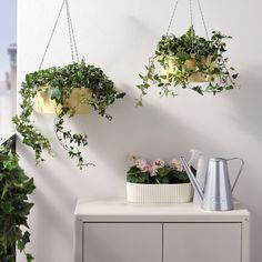 three hanging planters filled with green plants next to a white cabinet and sideboard