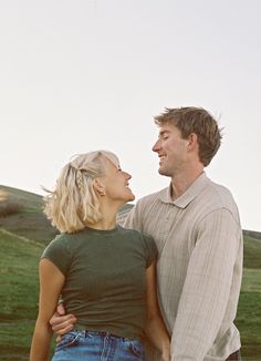 a man and woman standing next to each other in front of a field with green grass