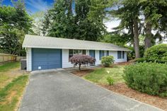 a house with blue garage doors and trees in the front yard, on a sunny day