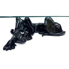 a glass table with two black cats on it's legs and one is laying down