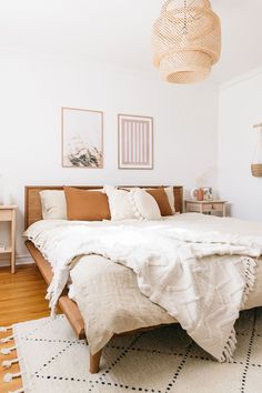 a bed with white sheets and pillows in a bedroom next to a wooden floor lamp