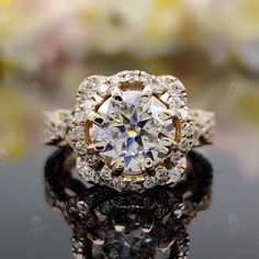 a diamond ring sitting on top of a black surface with flowers in the back ground