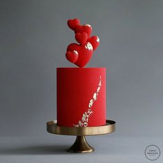 a red cake topped with hearts on top of a gold plated metal stand against a gray background