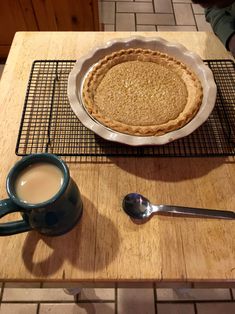 a pie sitting on top of a wooden table next to a cup of coffee and spoon