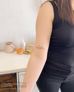 a woman with a small tattoo on her arm standing in front of a dresser and mirror