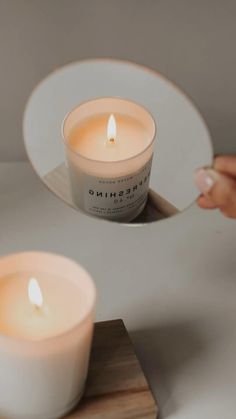 two white candles sitting on top of a wooden tray