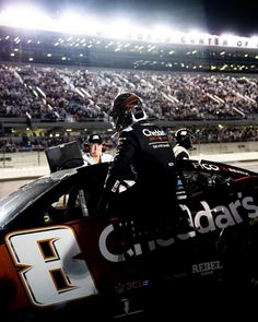 a man sitting on the back of a racing car in front of a large crowd