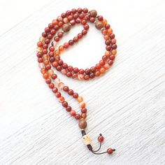 Let the fire of Sardonyx ignite your awareness with this handcrafted mala necklace.  Made in Kathmandu with 108 Sardonyx Fire Agate beads, four Bodhi Seed accents, and finished with a skull made of hand carved bone.  This mala is a meditation on the fleeting nature of existence and the freedom that comes from embracing life's journey and our impermanence.   The fiery Sardonyx inspires you to burn brightly and cherish each day, as even the the brightest flame will one day fade.  It reminds you to Handmade Red Mala For Healing, Red Handmade Mala For Healing, Red Mala With 108 Beads For Rituals, Red Hand-strung Spiritual Beaded Necklaces, Spiritual Agate Mala For Meditation, Spiritual Agate Mala With 108 Beads, Adjustable Hand-strung Agate Mala, Red Hand-strung Spiritual Mala, Adjustable Agate Hand-strung Mala