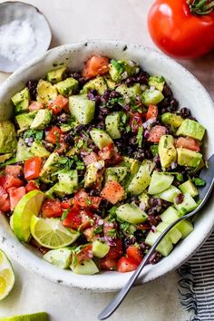 a white bowl filled with black beans, avocado and tomatoes next to sliced limes