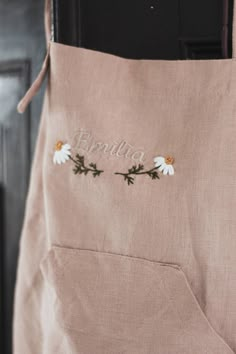 the back of a pink apron with daisies embroidered on it's front pocket