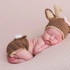 a newborn baby wearing a crocheted deer hat and diaper is sleeping on a blanket