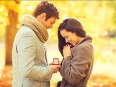 a man and woman standing next to each other in front of trees with autumn leaves