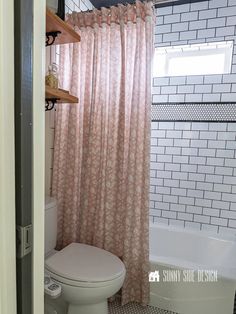 a white toilet sitting next to a bath tub in a bathroom under a window with pink curtains