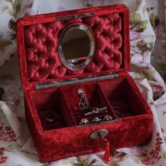 an open red velvet jewelry box sitting on a floral print tablecloth with a mirror in it