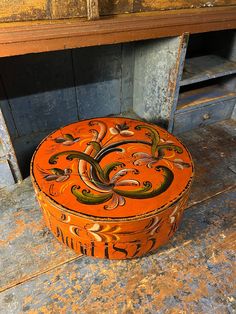 an orange box sitting on the ground in front of a wooden table with drawers and shelves