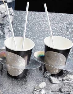 two cups with straws in them sitting on a table next to rocks and ice