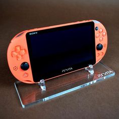 an orange sony vita is displayed on a brown surface with clear acrylic stand