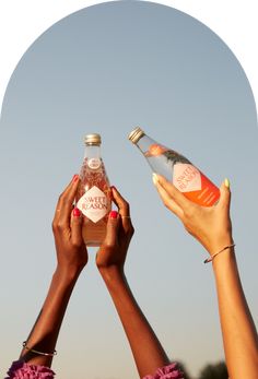 two women holding up bottles in the air with their hands on top of each other