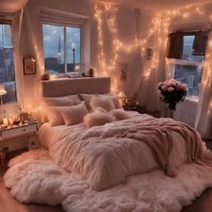 a bedroom with lights strung over the windows and a bed covered in fluffy white blankets