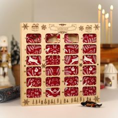 a wooden calendar with red and white designs on it, sitting on a table next to some candles