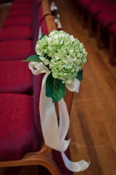 a bouquet of hydrangeas tied to the back of a wooden bench in a church