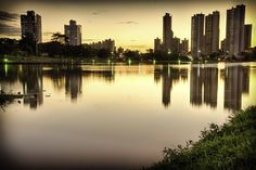 a body of water with tall buildings in the background at sunset or dawn, near grass and trees