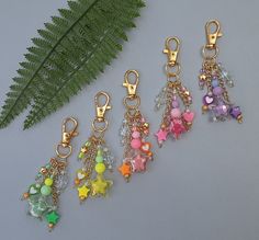 four charms with different colors and designs hanging from them next to a green fern leaf