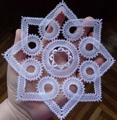 a hand holding a small white doily with holes in it's center and two fingers on the other side