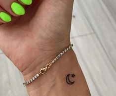 a woman's wrist with a yellow manicure and a crescent tattoo on it