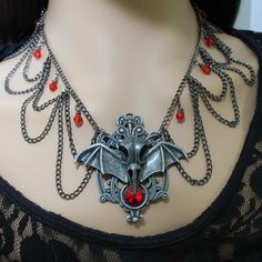 This elaborate gothic necklace features a large raven skull with bat wings, three draping layers of gunmetal toned chain and blood red, top quality, crystal beads. The pendant measures 2.5" tall and 3" wide and is made of sturdy oxidized metal. It holds a 12mm round glass gemstone. The necklace chain is 16" to 18" adjustable, but I can make it longer upon request. The necklace would look great with a vampiric styled gown (especially for Halloween), gothic styled robes, steampunk attire or a simp