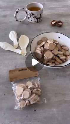 a white bowl filled with lots of wooden slices next to a cup of tea and spoons