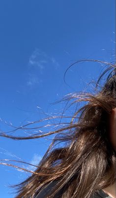 a woman with her hair blowing in the wind while looking up at a blue sky