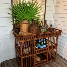 a wooden shelf with bottles and baskets on it in front of a white house next to a palm tree