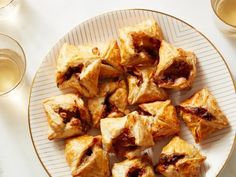 a white plate topped with lots of pastries next to glasses of water and wine