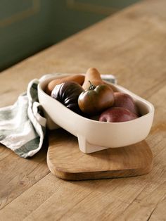 a white bowl filled with assorted vegetables on top of a wooden table next to a towel