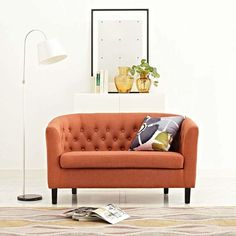 an orange couch sitting in front of a white wall with a lamp next to it