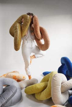 a woman in white jumpsuits surrounded by stuffed animals and pillows on the floor