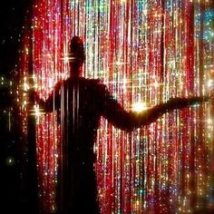 a man is standing in front of a curtain with lights all around him and his arms are out