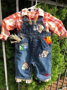 an infant's jean overalls and plaid shirt are hanging on a fence outside