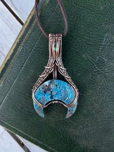 This unique wire wrapped Moss Agate moon pendant with mystic quartz was made to be reminiscent of the Earth's beauty, including blue and green hues representing water and grass. Hand made with care, this pendant is intricately woven from copper wire and is meticulously crafted to create a celestial-inspired essence. Whether you're a nature lover, a spiritual seeker, or just appreciate artisanal craftsmanship, this pendant is the perfect addition to your jewelry collection. Wear it as a symbol of your connection to the Earth or gift it to someone special who shares your love for the natural world. Comes finished with a brown faux (vegan) suede band with lobster clasp closure.  Features: crescent moon with shimmering green mystic quartz  Materials: copper wire, moss agate Style: Earth inspir Wire Wrap Crescent Moon Pendant, Luxury Wire Wrapped Round Pendant Necklace, Wire Wrap Triangle Stone, Handmade Mystical Blue Jewelry, Handmade Mystical Agate Jewelry, Turquoise Wire Wrapped Crystal Necklace For Healing, Artisan Wire Wrapped Chrysocolla Jewelry, Bohemian Moss Agate Jewelry Wire Wrapped, Blue Hand Forged Jewelry For Healing