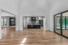 an empty living room with wood floors and glass doors leading to the kitchen, dining area and outdoor swimming pool