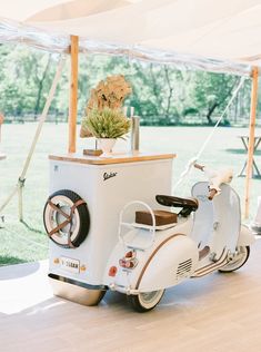 an old fashioned scooter is parked under a tent with flowers in the back