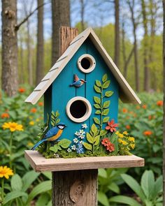 a blue birdhouse sitting on top of a wooden post in a forest filled with flowers